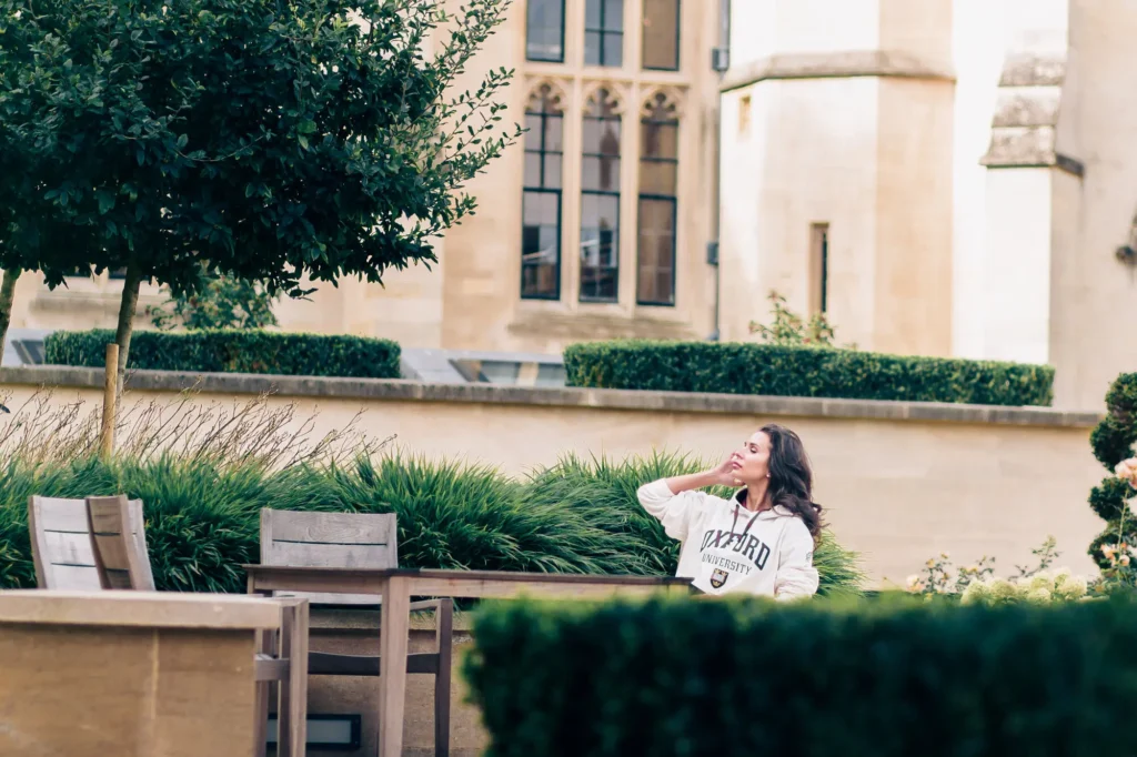 Oxford graduate in a university hoodie relaxing in the Magdalen College gardens