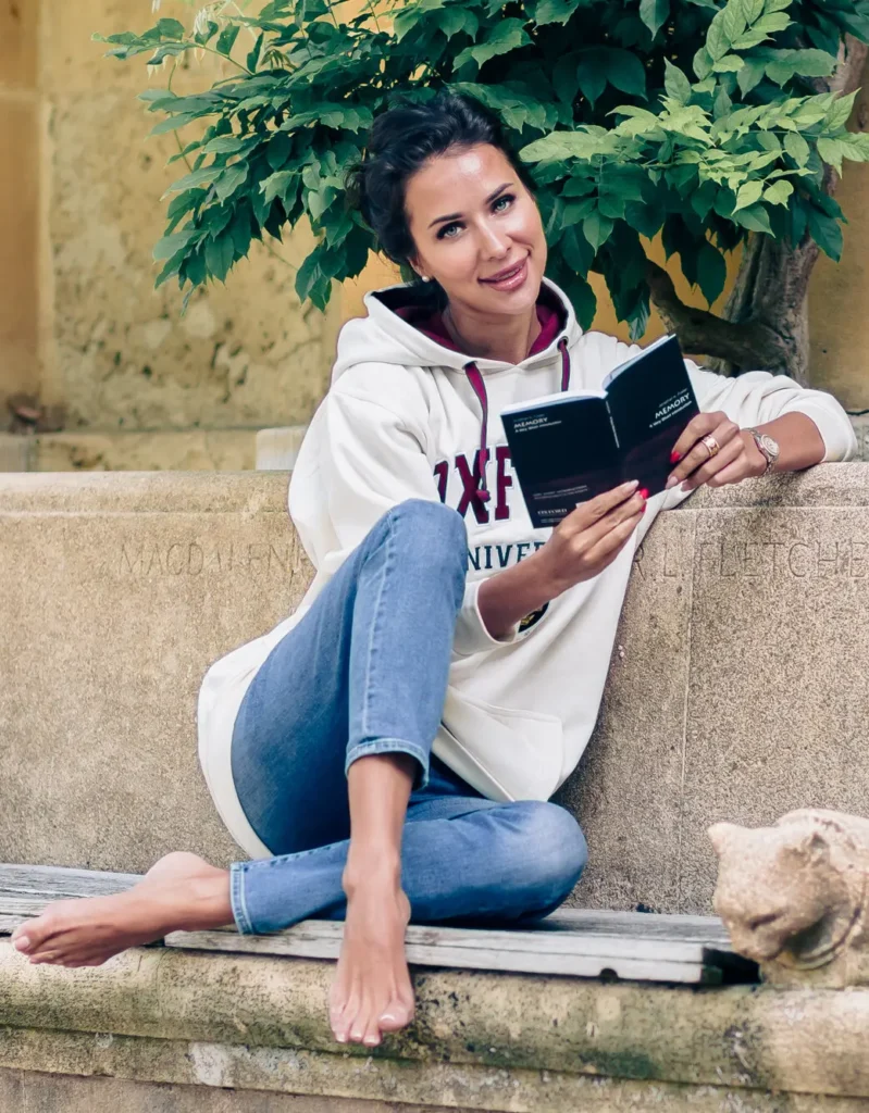 Barefoot Oxford graduate reading on a stone bench at Magdalen College during a graduation photoshoot