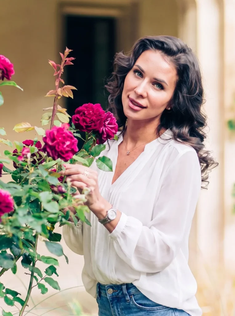 Close-up portrait of a smiling woman beside deep pink roses at Magdalen College, Oxford