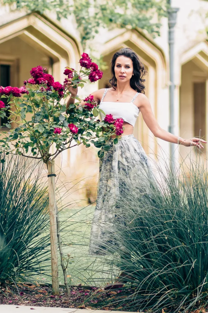 Woman in printed maxi skirt standing beside rose bushes in a Magdalen College courtyard, Oxford