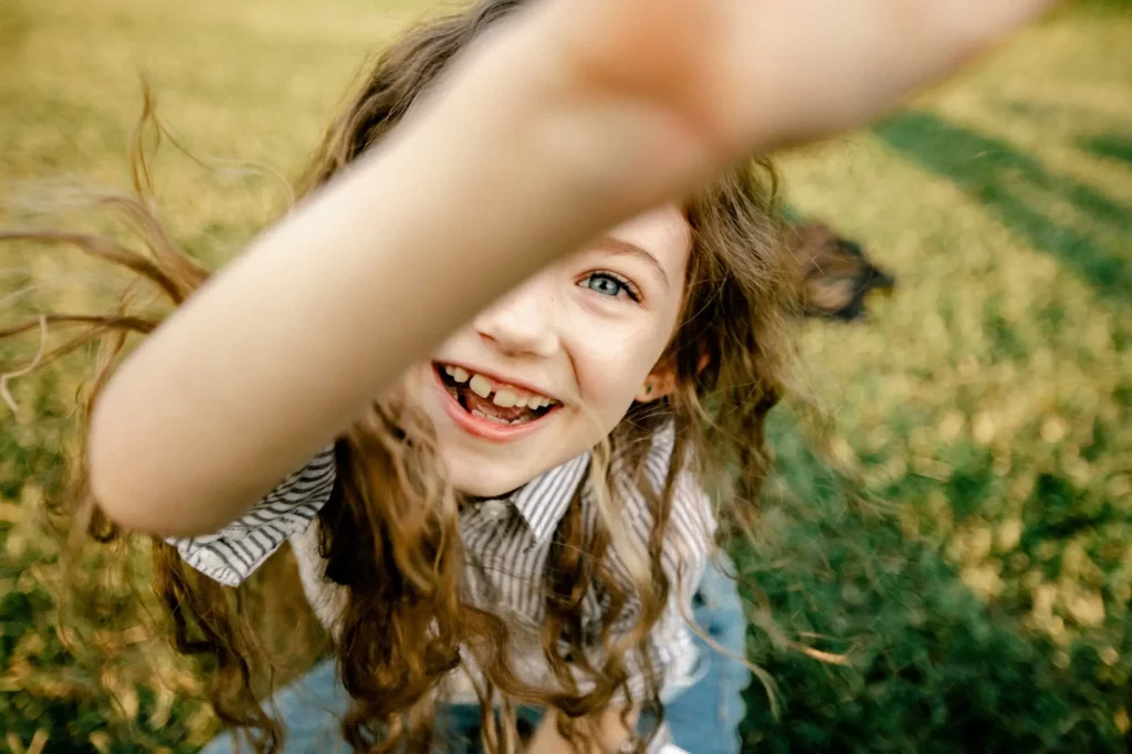 Close-up of a girl laughing with her arm reaching toward the camera, Oxford children photographer at University Parks