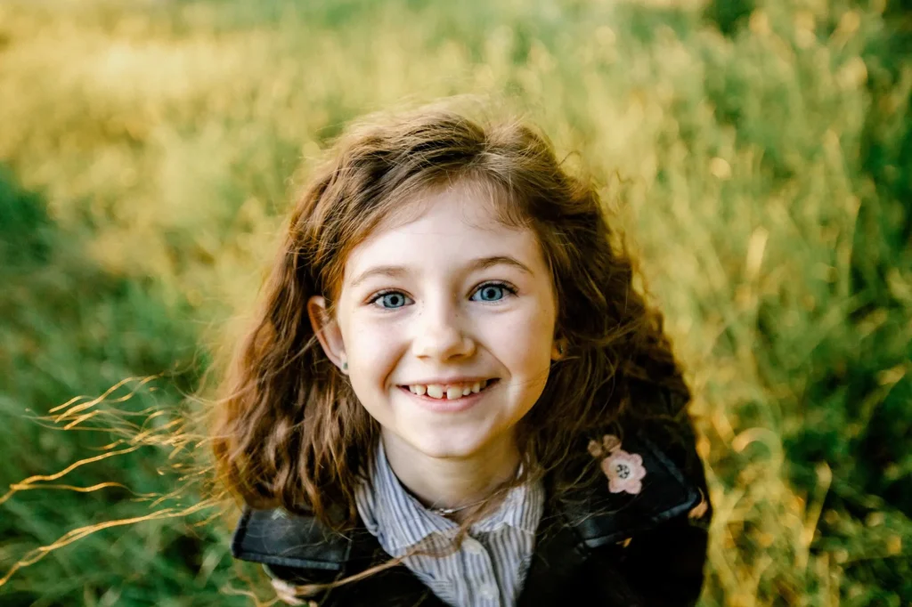 Close-up portrait of a smiling girl with blue eyes and a gappy smile, Oxford children photographer at University Parks