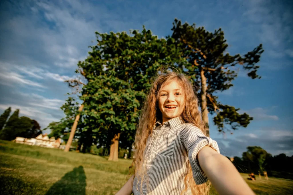 Girl reaching toward the camera under a large tree against a blue sky, Oxford children photography at University Parks