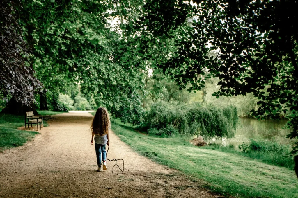 Young girl walking away along a riverside path holding a stick, Oxford children photography at University Parks
