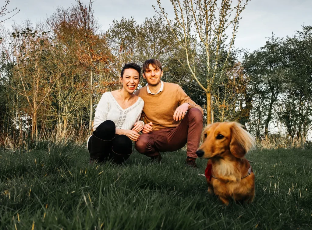 Couple crouching in the countryside with their dachshund, candid Oxford engagement photography