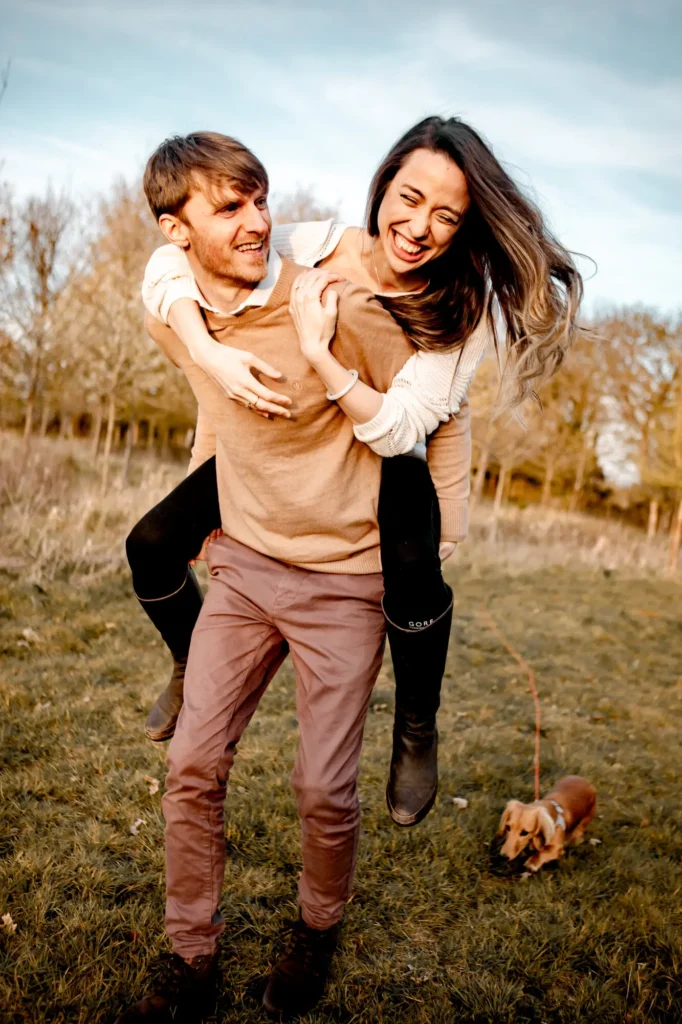 Man giving his fiancée a piggyback ride through a field, candid Oxford engagement photography