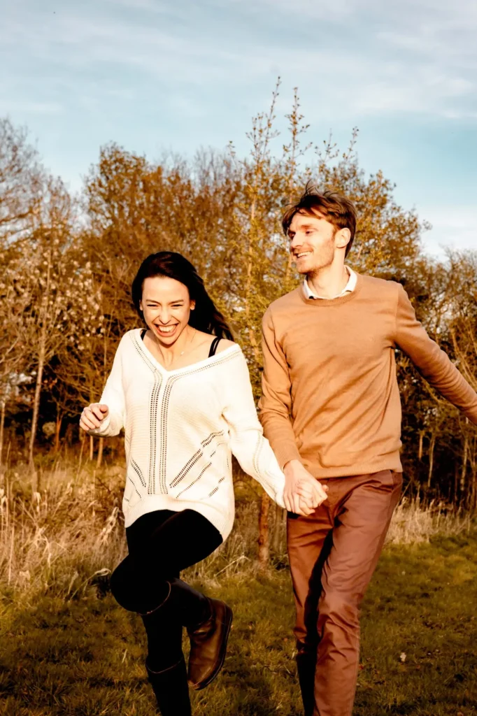 Couple laughing while walking hand in hand through an autumn field during an Oxford engagement photoshoot