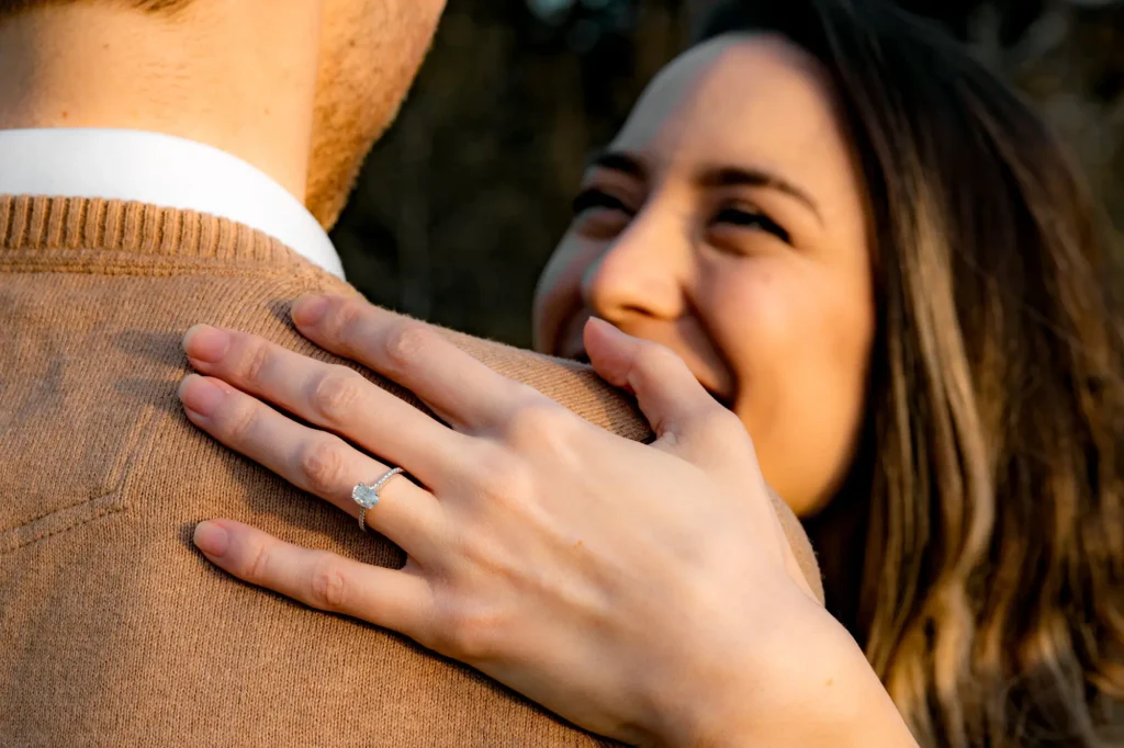 Close-up of an engagement ring on a woman's hand resting on her partner's shoulder