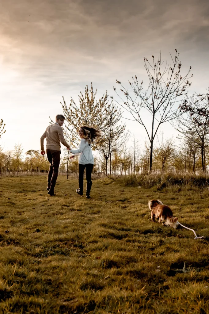 Couple running together through an autumn field with their dog, Oxfordshire engagement shoot