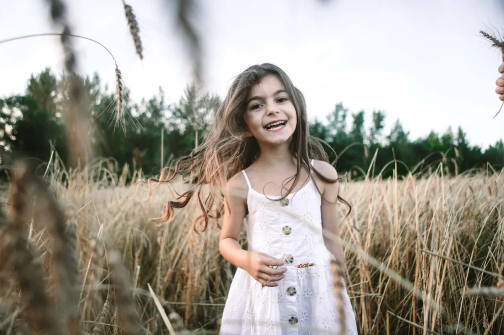 Young girl laughing among wheat stalks with a hand reaching in at the frame's edge, Oxford family photographer
