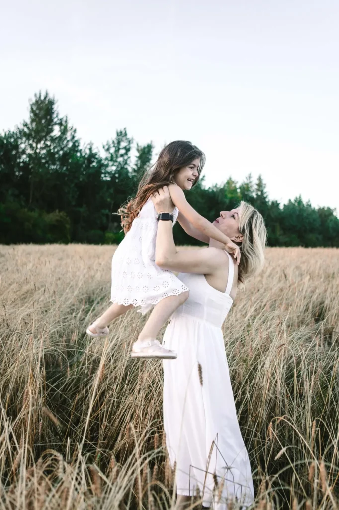 Mother lifting her laughing daughter into the air in a wheat field, Oxford family photographer