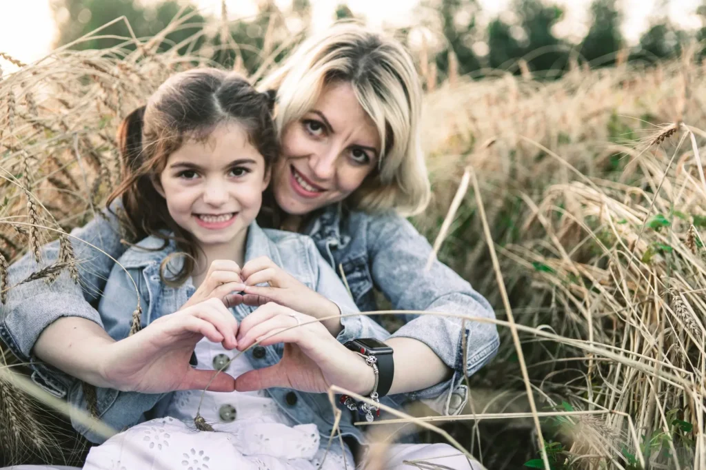 Mother and daughter making a heart shape with their hands together in a wheat field, Oxford family photography