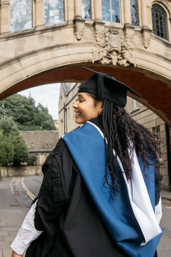 Close-up of a graduate in cap and gown smiling beneath the Bridge of Sighs arch