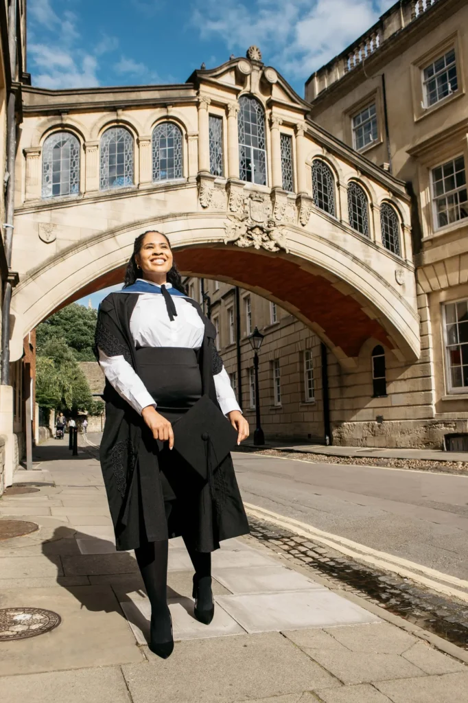 Graduate holding her mortarboard on New College Lane beneath the Bridge of Sighs