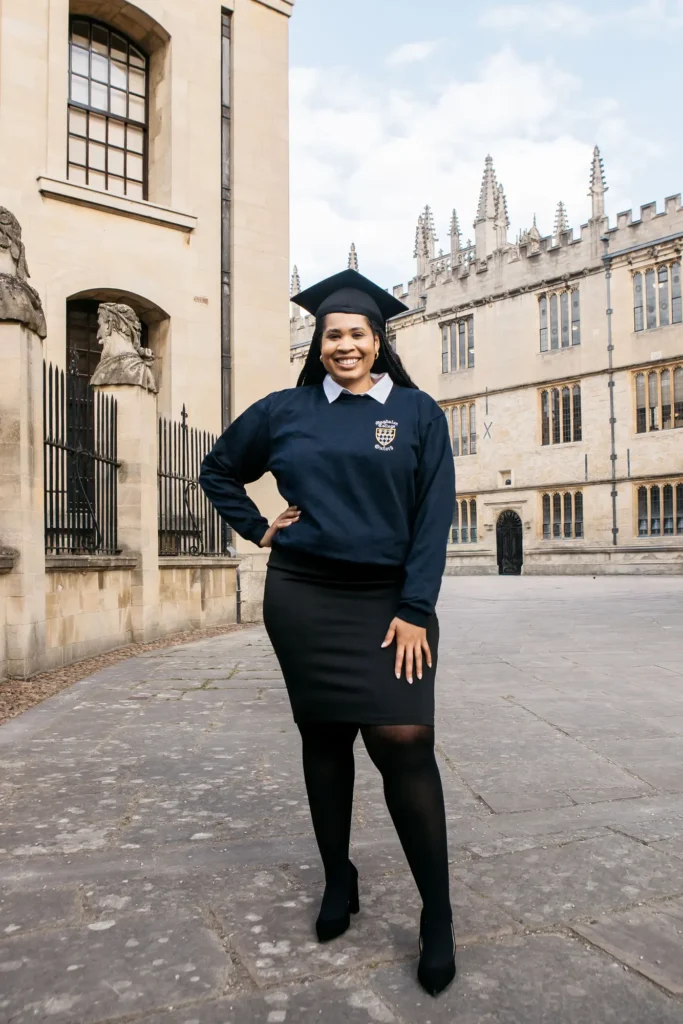 Magdalen College graduate in college jumper and mortarboard in the Bodleian's Old Schools Quad