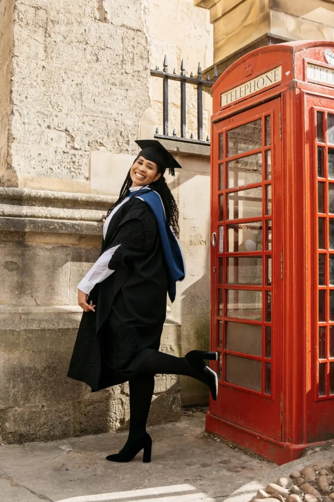 Oxford graduate laughing beside a classic red telephone box near Radcliffe Square