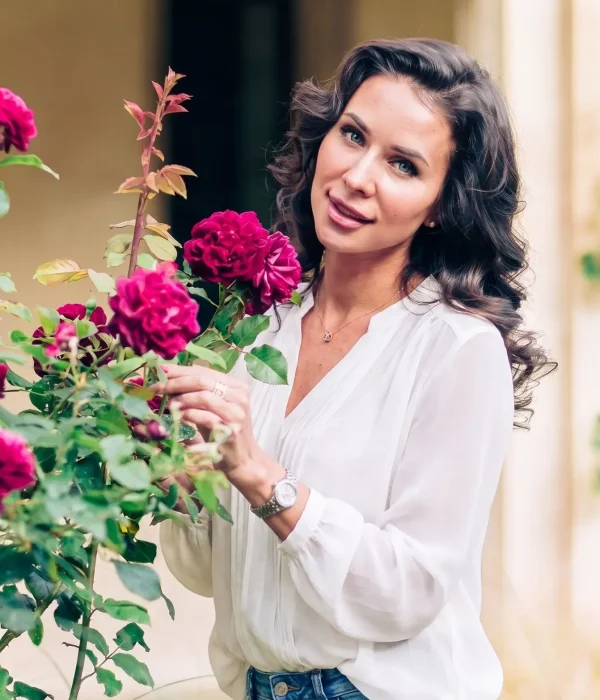 Close-up portrait of a smiling woman beside deep pink roses at Magdalen College, Oxford